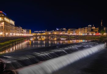 Beautiful nighttime scenery of Florence's Arno River with illuminated buildings and bridge reflections.