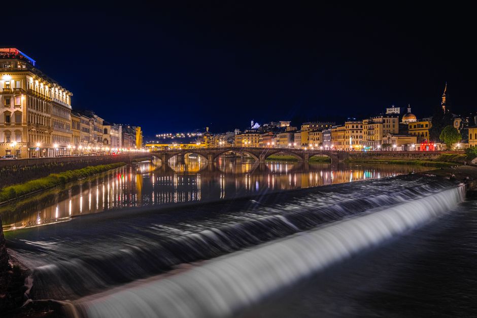 Beautiful nighttime scenery of Florence's Arno River with illuminated buildings and bridge reflections.