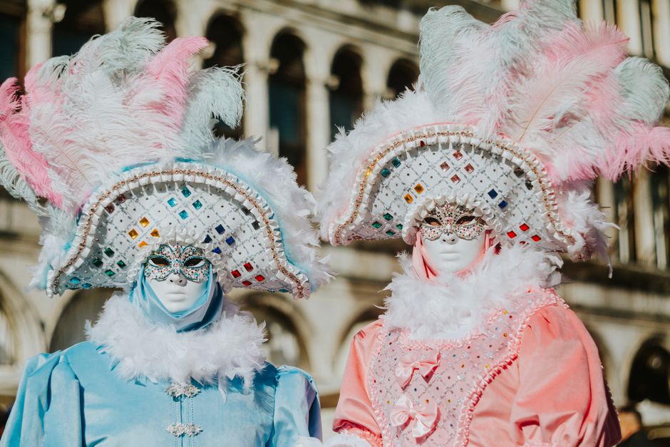 Two individuals in ornate Venetian masks and costumes pose during a carnival.