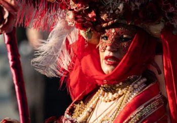 An adult wearing an ornate red masquerade costume and mask at a themed festival.