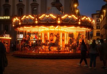 A beautifully illuminated carousel spinning at night in a lively urban square in Florence, Italy.