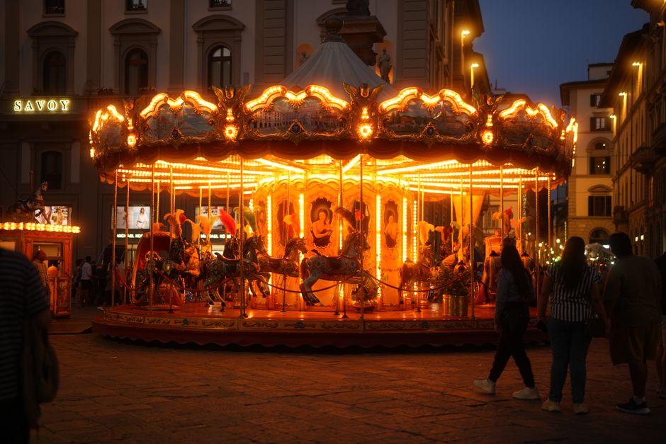 A beautifully illuminated carousel spinning at night in a lively urban square in Florence, Italy.