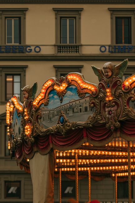 Intricate carousel with ornate details in front of historic building in Florence, Italy.