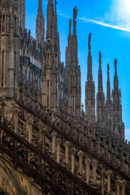 Detailed view of the ornate spires at Milan's iconic Duomo, showcasing Gothic architecture against a clear blue sky.