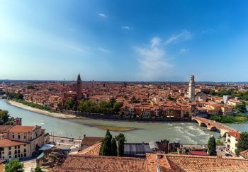 Stunning aerial view of Verona cityscape, featuring the Adige River winding through historic architecture under a clear blue sky.