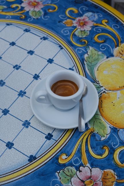 A cup of espresso on a vibrant Sicilian ceramic table in Cefalù, Italy.