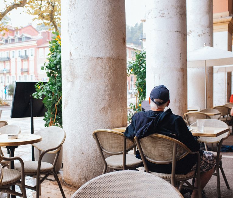 A senior man enjoying a quiet moment at an outdoor cafe with a city view.