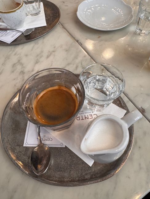 A shot of espresso with a jug of milk and water on a cafe table in Budapest.
