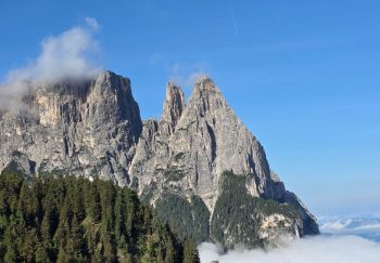 Breathtaking view of the Dolomites above a forest with mist and blue sky.