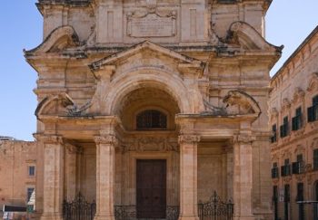 Stunning Baroque church facade lit by bright sunlight in an empty plaza.