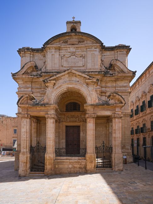 Stunning Baroque church facade lit by bright sunlight in an empty plaza.