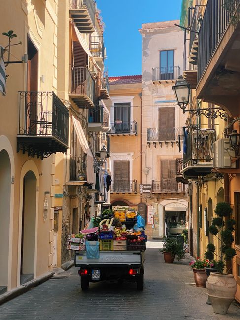 Picturesque Cefalù street in Sicily featuring a fruit-laden cart amidst historic buildings.