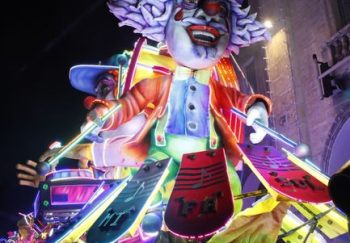 Colorful lit carnival float featuring a clown, drawing crowds at night.