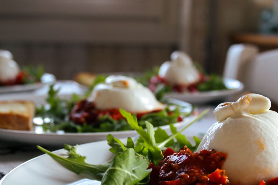 A close-up of burrata cheese with tomato relish and arugula on a plate, emphasizing Italian cuisine.