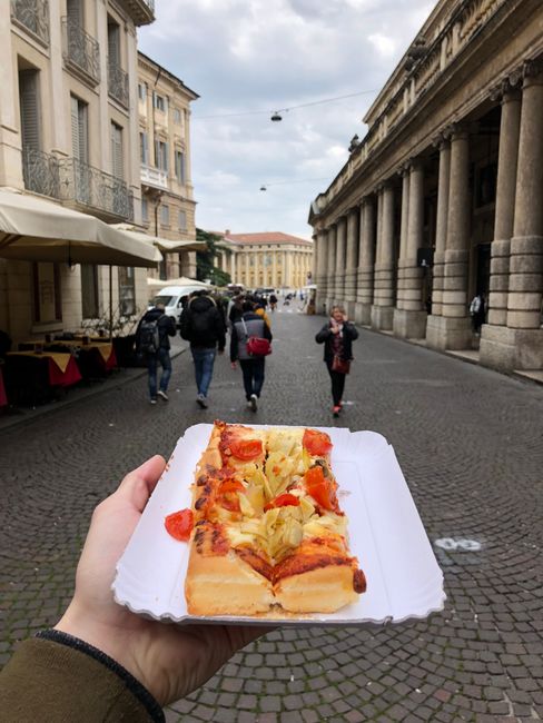 Enjoying a slice of delicious pizza on a bustling street in Verona, Italy.