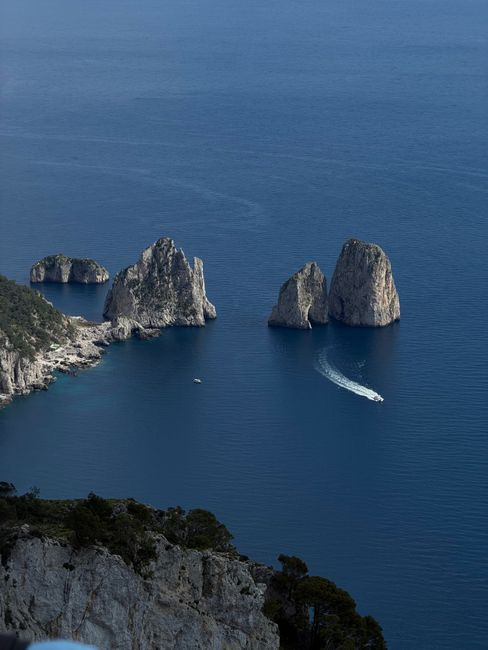Stunning aerial view of iconic Faraglioni rock formations in Capri, Italy, with a boat navigating the blue sea.