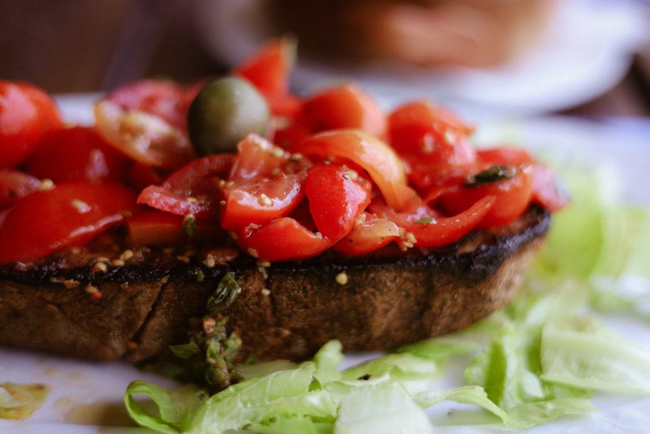 Close-up of traditional Italian bruschetta topped with cherry tomatoes and an olive.
