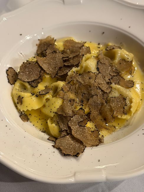 Close-up of creamy pasta topped with fresh shaved truffles on a white plate.