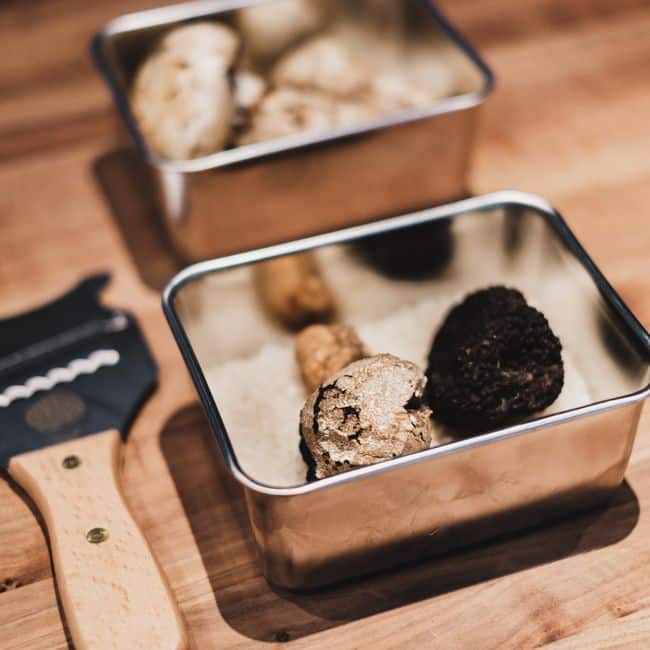 Close-up of assorted gourmet truffles in metal containers on a wooden counter.