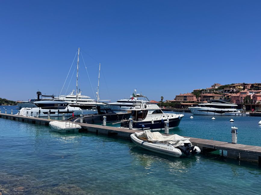Stunning view of luxury yachts docked at a marina in Porto Cervo, Sardinia, under a clear blue sky.