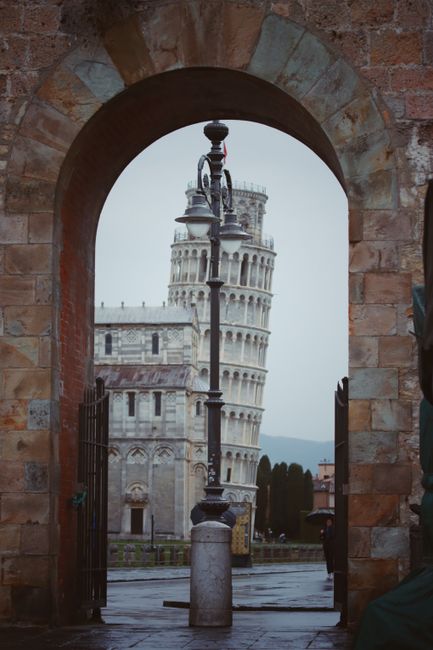 Iconic Leaning Tower of Pisa visible through a stone archway, symbolizing Italy's rich history.