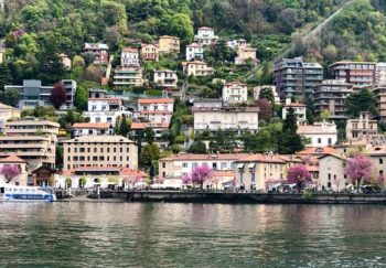 Picturesque view of a charming Italian town nestled by Lake Como, surrounded by lush green hills overlooking tranquil waters.