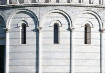 The Pisa Baptistery in Tuscany, Italy, featuring its ornate facade with a person seated for scale.