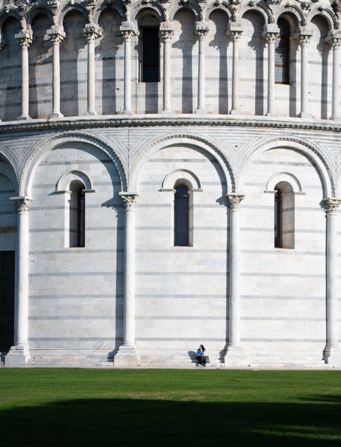 The Pisa Baptistery in Tuscany, Italy, featuring its ornate facade with a person seated for scale.