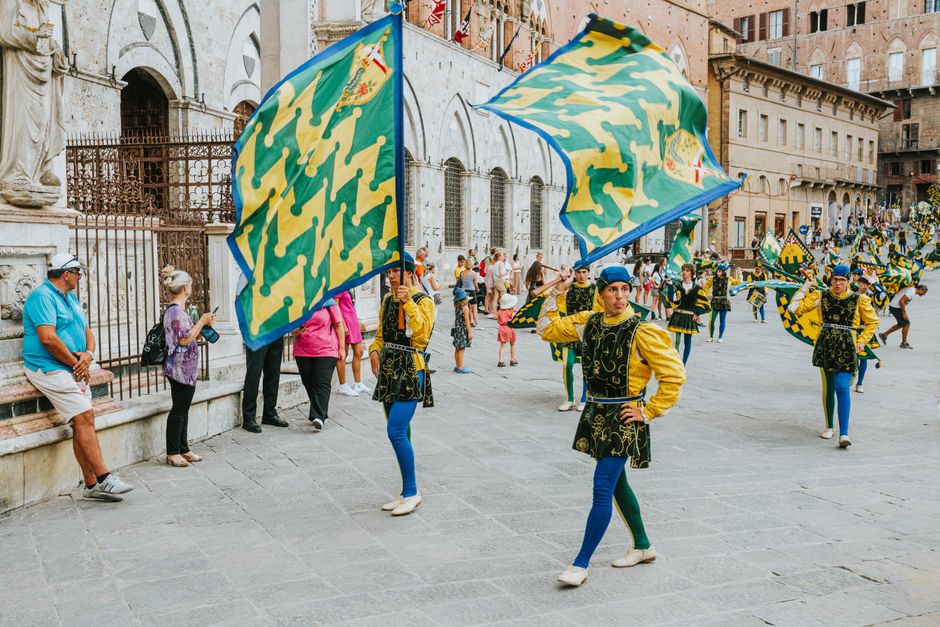Colorful traditional parade with flags in a historic European town street.