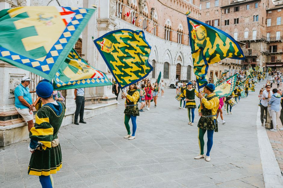 Vibrant street parade with flags and performers in historic square, capturing the lively festival atmosphere.