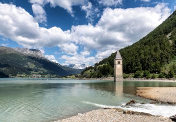 Picturesque view of Campanile di Curon submerged in Reschen Lake, surrounded by Alps.