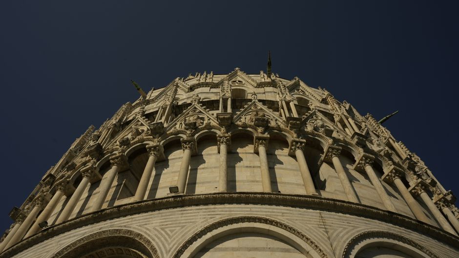 Close-up of the intricate stone architecture of Pisa Baptistery under clear skies.