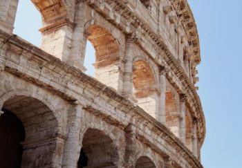 Detailed view of the Colosseum's ancient Roman architecture in Rome, Italy under clear blue skies.