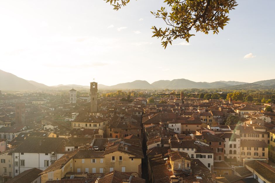 A stunning view of Lucca, Italy, showcasing historic architecture and mountains at sunset.