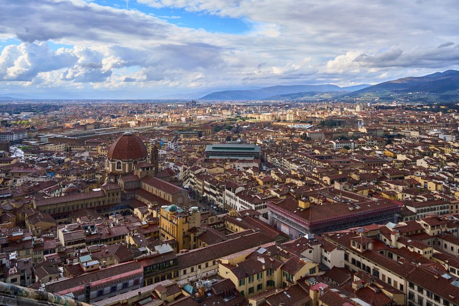 Stunning aerial view of Florence featuring iconic red rooftops and mountain backdrop under a cloudy sky.