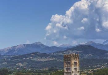 Beautiful landscape of Lucca, Italy featuring Torre Guinigi and surrounding mountains under a blue sky.