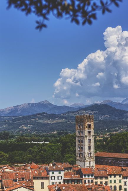 Beautiful landscape of Lucca, Italy featuring Torre Guinigi and surrounding mountains under a blue sky.
