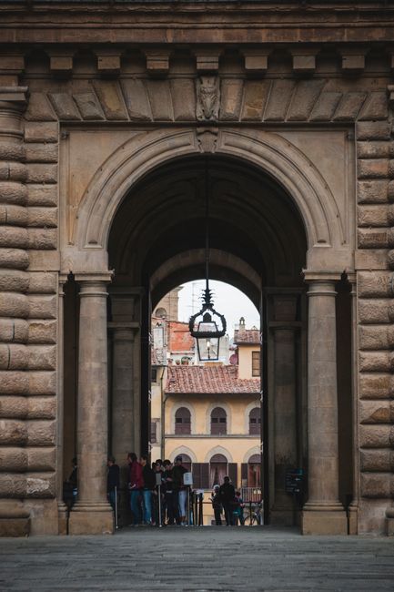 Group of people standing under scenic stone archway against old cozy houses in European city