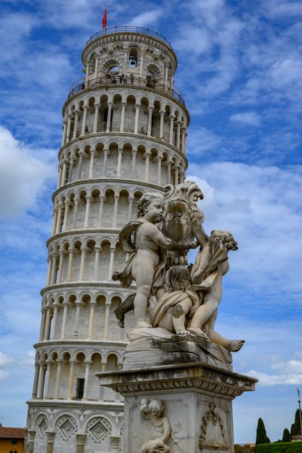 Iconic view of the Leaning Tower of Pisa with decorative cherub statues under a vibrant sky.
