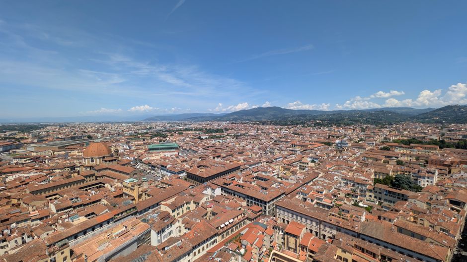 Breathtaking aerial shot of Florence's iconic red rooftops and landscape under a clear blue sky.