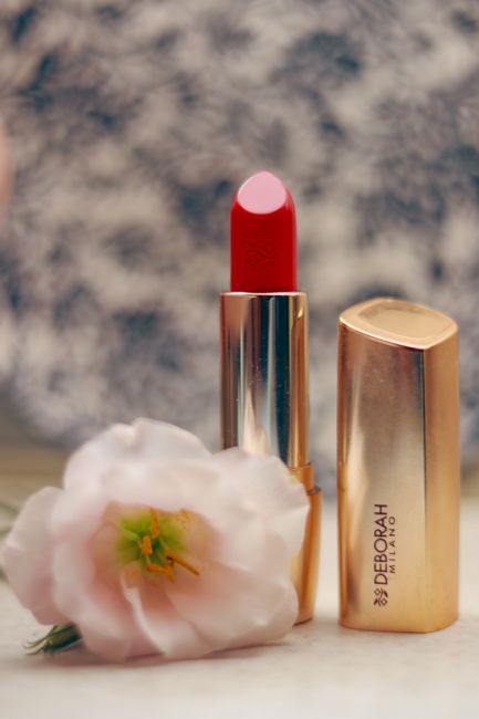 Red lipstick with gold packaging and a delicate flower, perfect for beauty layouts.