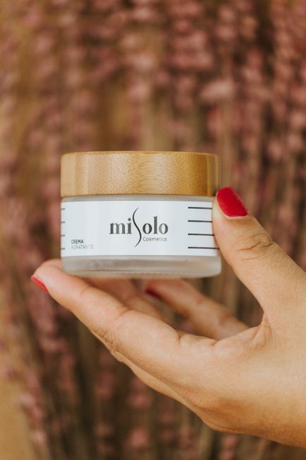 Close-up of a woman's hand holding a skincare cream jar with wooden lid, showcasing beautiful nails.