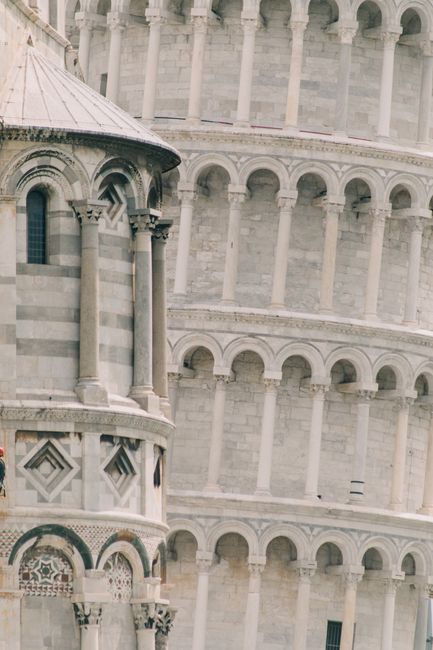 Exterior of aged stone cathedral with columns and carve details and leaning tower with pillars