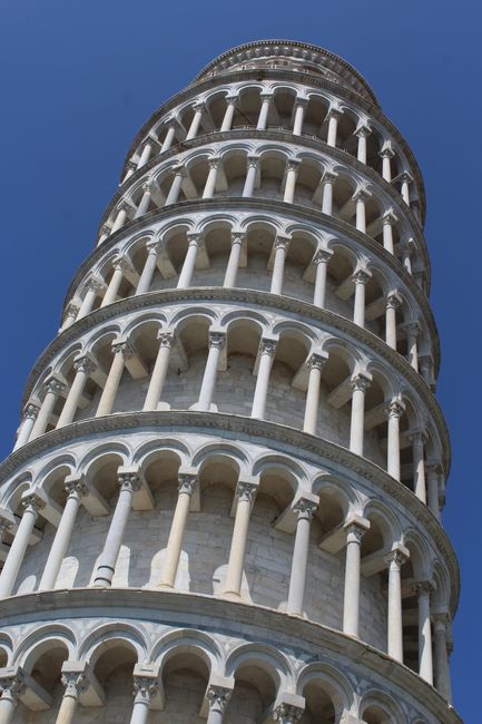 Low-angle view of the iconic Leaning Tower of Pisa in Italy against a clear blue sky.