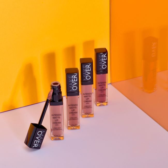 A stylish arrangement of intense matte lip creams against a vibrant orange backdrop, showcasing beauty and elegance.