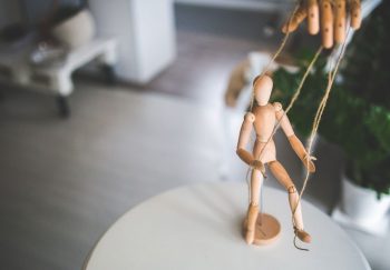 Close-up of a wooden marionette controlled by strings indoors. Artistic representation of control and manipulation.