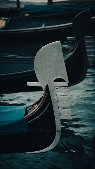 Close-up of a classic Venetian gondola prow in soft lighting on calm water.