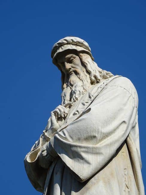 A classic low-angle view of Leonardo da Vinci statue with a clear blue sky background.