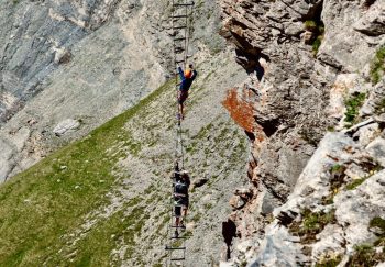 Daredevil climbers tackle a challenging ladder across a steep mountain face.