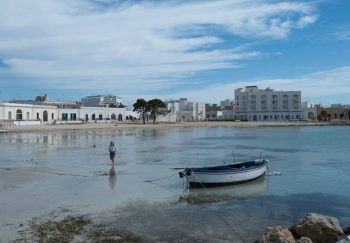 Peaceful seaside view with a moored boat and coastal buildings in Salento, Italy.
